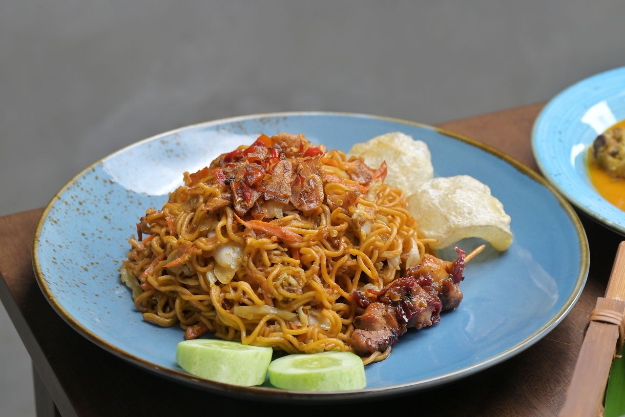 A mouthwatering plate of authentic Indonesian mie goreng garnished with cucumbers and crackers.