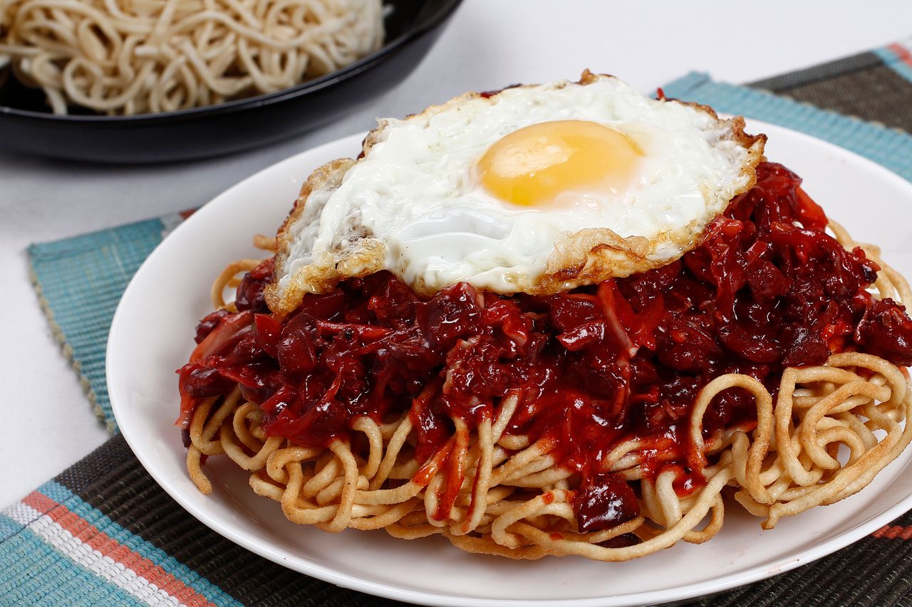 Mouth-watering Mie Goreng with spicy red sauce topped with a fried egg, perfect for Asian cuisine lovers.